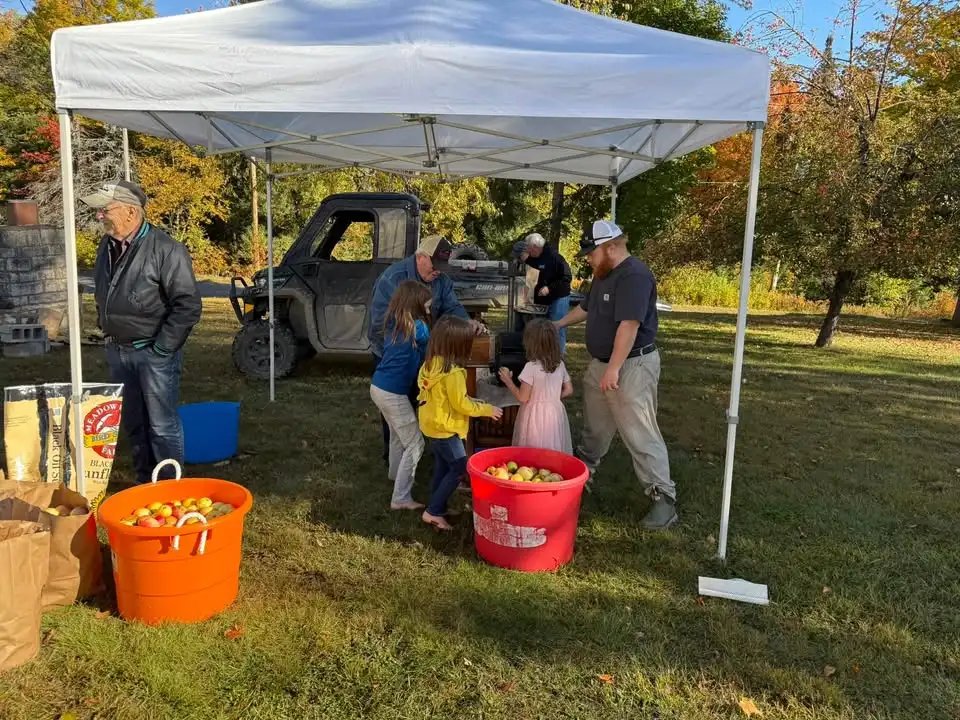 Families and children pressing fresh apple cider outdoors under a tent at the Beechwood Apple Festival